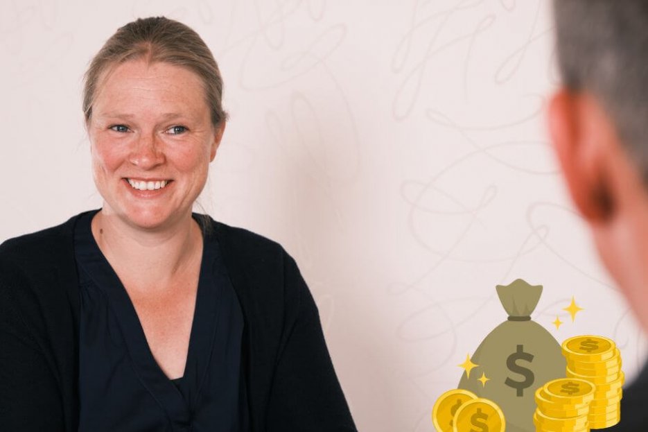 Auf diesem Foto bin ich als Coach zusammen mit einem Kunden zu sehen. Ich lächel freundlich, mein Kunde ist von hinten zu sehen. Er hat kurze dunkelblonde Haare. Ich habe lange dunkelblonde Haare, die zurückgebunden sind. Er trägt ein schwarzes Poloshirt. Ich trage eine blaue Bluse und eine blaue Strickjacke. Neben meinem Kunden sind als Comicbild Münzen und ein kleiner Geldsack zu sehen.