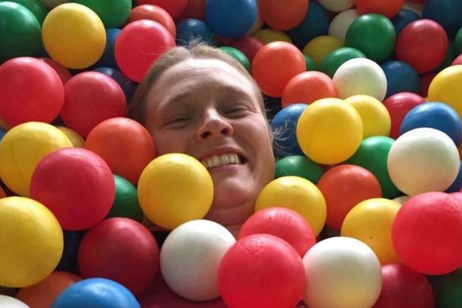 Ich bin im Bällebad zu sehen. Eine dunkelblonde Frau in bunten Bällen. Von mir ist nur der Kopf zu sehen, der Rest ist unter den Bällen versteckt. Ich lache.