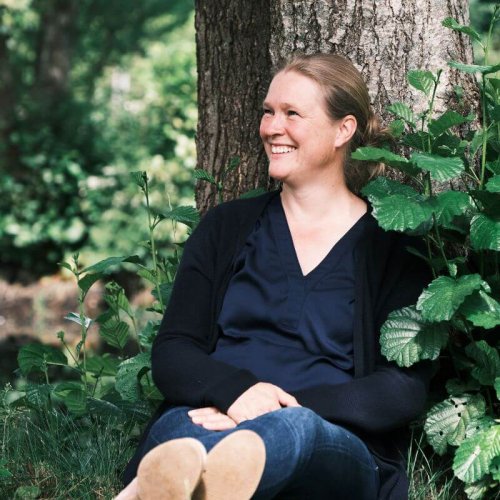 Auf diesem Foto bin ich abgebildet. Ich sitze an einen Baum gelehnt und lächle.