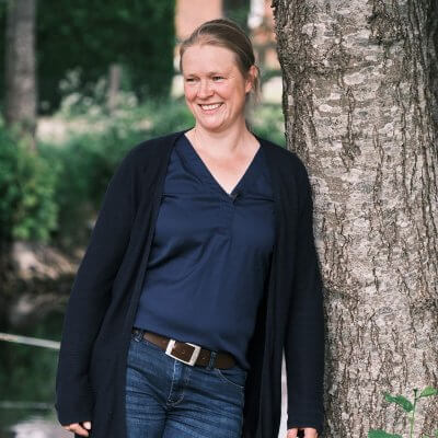 Ich stehe an einen Baum gelehnt. Mit der linken Schulter. Ich lächle. Ich trage blaue Klamotten. Jeans, Bluse, Strickjacke. Mein Haar ist dunkelblond und zu einem Knoten geflochten.
