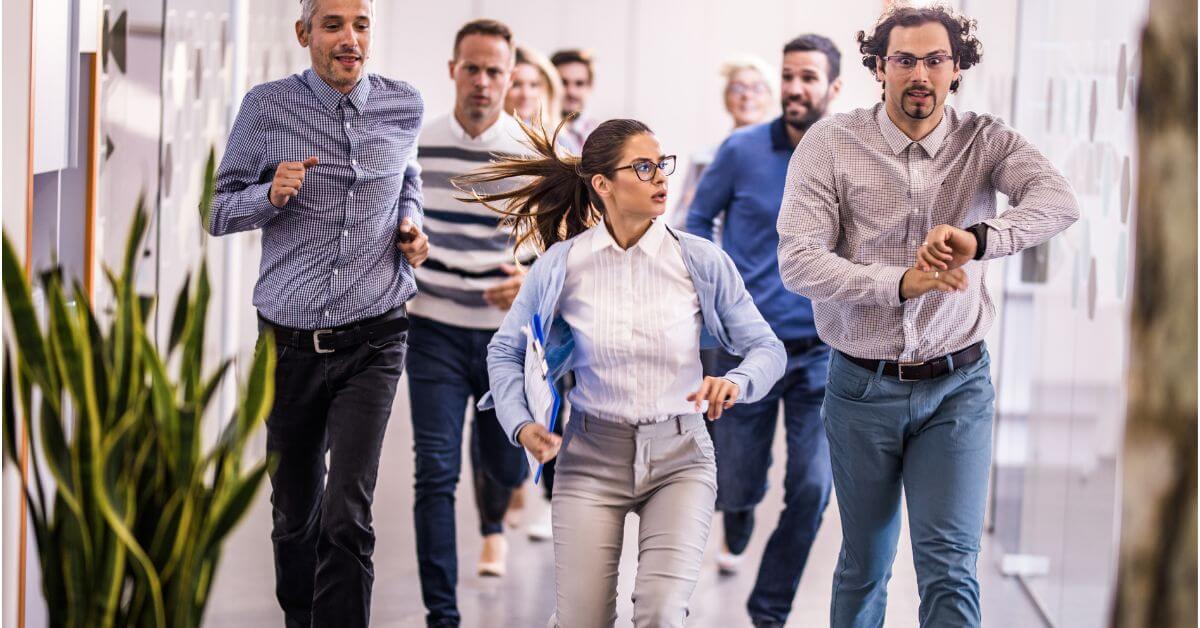 Es sind Menschen auf dem Flur zu sehen, die hektisch auf die Uhr schauen und sich beeilen. Männer und Frauen.