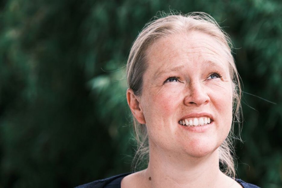 Auf dem Bild bin ich zu sehen. Ich schaue etwas fragend in den Himmel. Hinter mir ist ein grüner Busch zu erahnen. Er ist verschwommen.