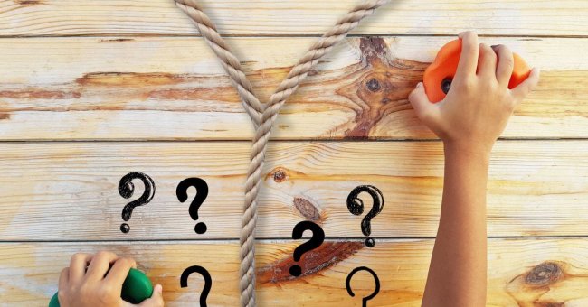Das Foto zeigt ein Seil, dass sich trennt, zwei Hände an Bouldergriffen und viele Fragezeichen. Das Seil ist beige, die Fragezeichen schwarz, der linke Bouldergriff grün, der rechte orange. Im Hintergrund ist eine Holzwand zu erkennen, an der die Griffe befestigt sind.