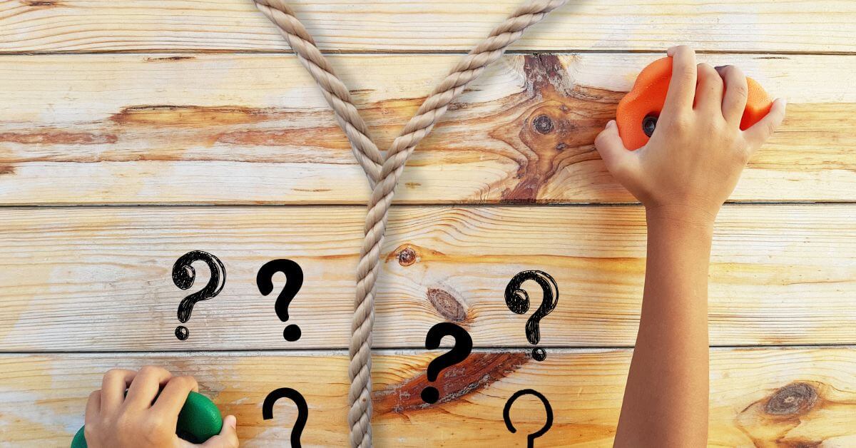 Das Foto zeigt ein Seil, dass sich trennt, zwei Hände an Bouldergriffen und viele Fragezeichen. Das Seil ist beige, die Fragezeichen schwarz, der linke Bouldergriff grün, der rechte orange. Im Hintergrund ist eine Holzwand zu erkennen, an der die Griffe befestigt sind.