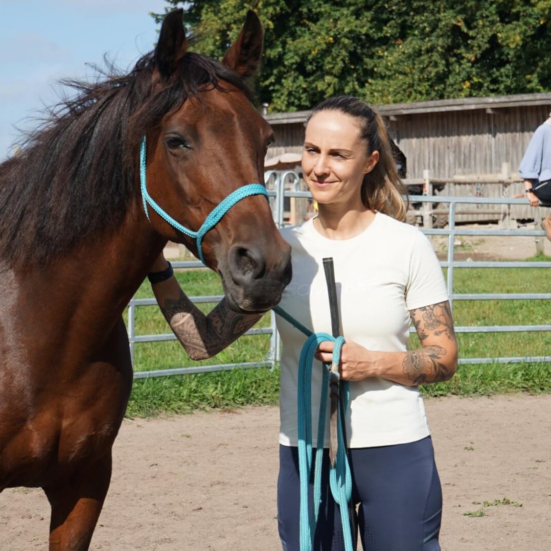 Hier siehst du das Pferd Butterfly mit ihrer Schülerin. Beide sehen entspannt aus. Butterfly ist ei ne braune Stute mit schwarzer Mähne. Sie trägt ein türkises Halfter.