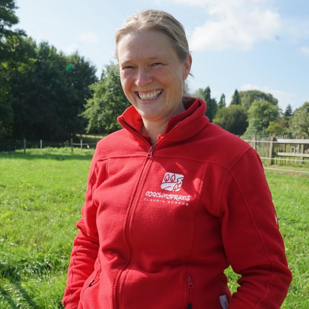 Auf diesem Foto siehst du mich, strahlend lachen. Ich trage eine rote Fleecejacke mit dem Firmenlogo "Coachingpraxis Claudia Süsens"
