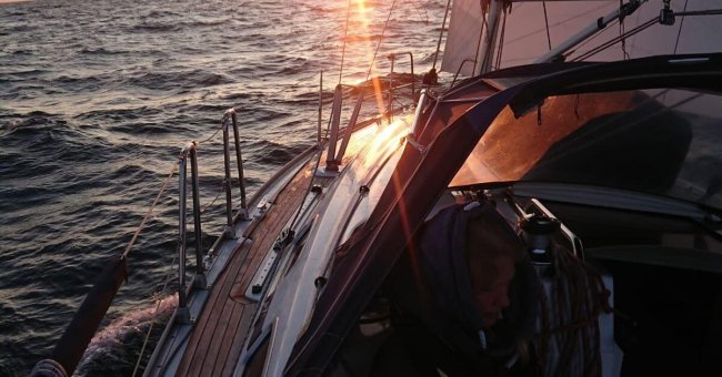 Ausschnitt eines Segelbootes. Es ist die Reeling zu erkennen und es ist zu erahnen, dass die Sonne gerade untergeht.