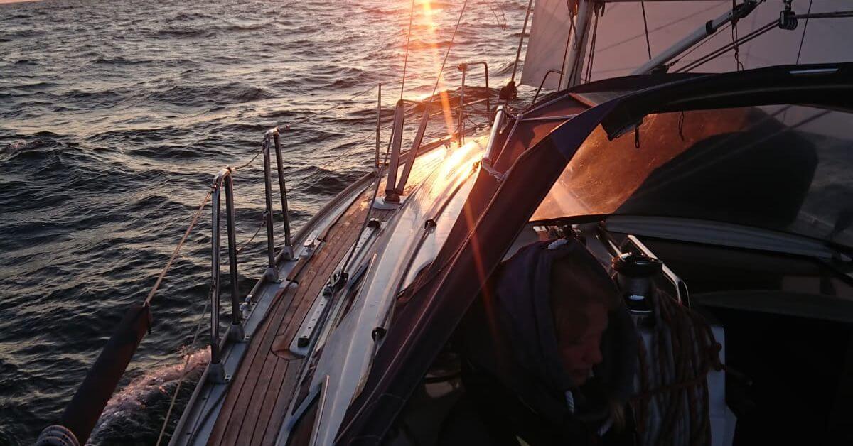 Ausschnitt eines Segelbootes. Es ist die Reeling zu erkennen und es ist zu erahnen, dass die Sonne gerade untergeht.