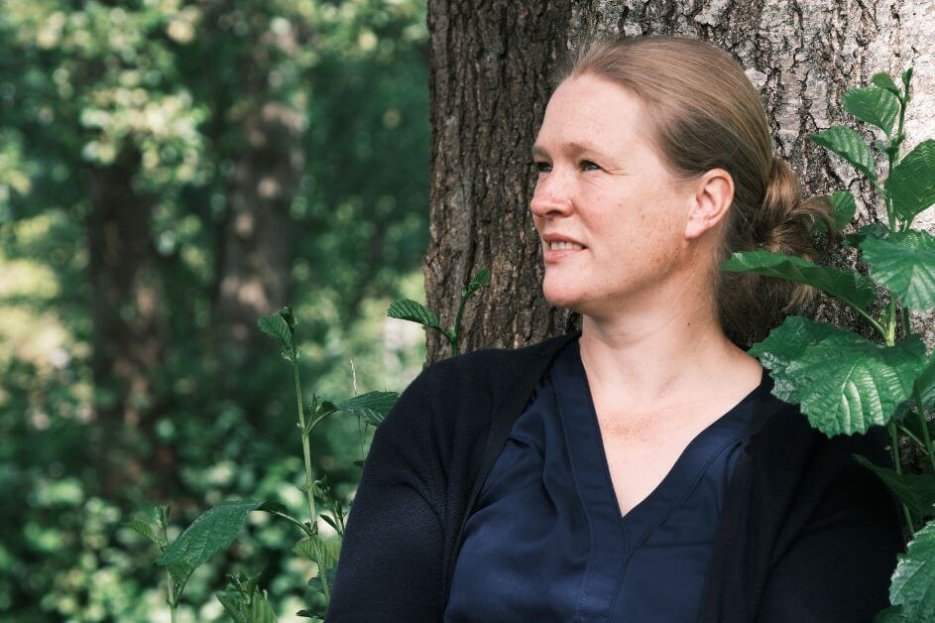 Ich sitze an einen Baum gelehnt und schaue nachdenklich in die Ferne. Es scheint Sommer zu sein, denn das Laub des Baumes ist dunkelgrün. Ich trage eine Strickjacke und eine Bluse, beides in dunkelblau