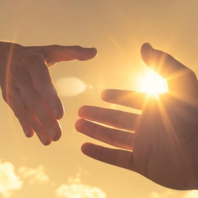 Es sind zwei Hände abgebildet, die sich gerade loslassen oder gleich festhalten. Der Hintergrund ist ein gelblicher Himmel und eine Sonne. Vielleicht ein Sonnenuntergang.