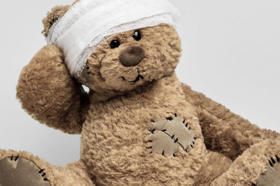 Auf diesem Foto ist ein Teddybär abgebildet, der einen Kopfverband trägt und ein Pflaster auf dem Herzen hat.