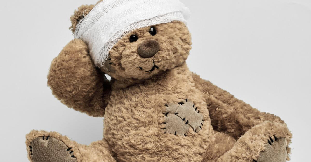 Auf diesem Foto ist ein Teddybär abgebildet, der einen Kopfverband trägt und ein Pflaster auf dem Herzen hat.