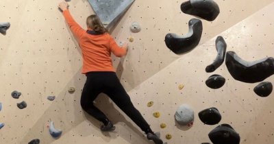 Hier bin ich beim Bouldern abgebildet. Ich trage eine schwarze Jogginghose und eine orangene Fleecejacke.